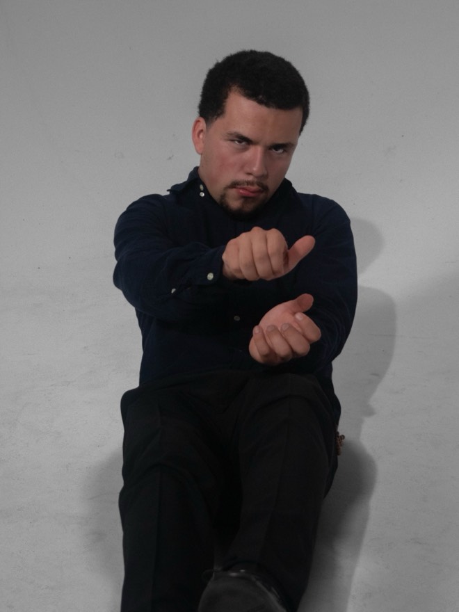 Uriel sitting on the studio floor pointing at the camera